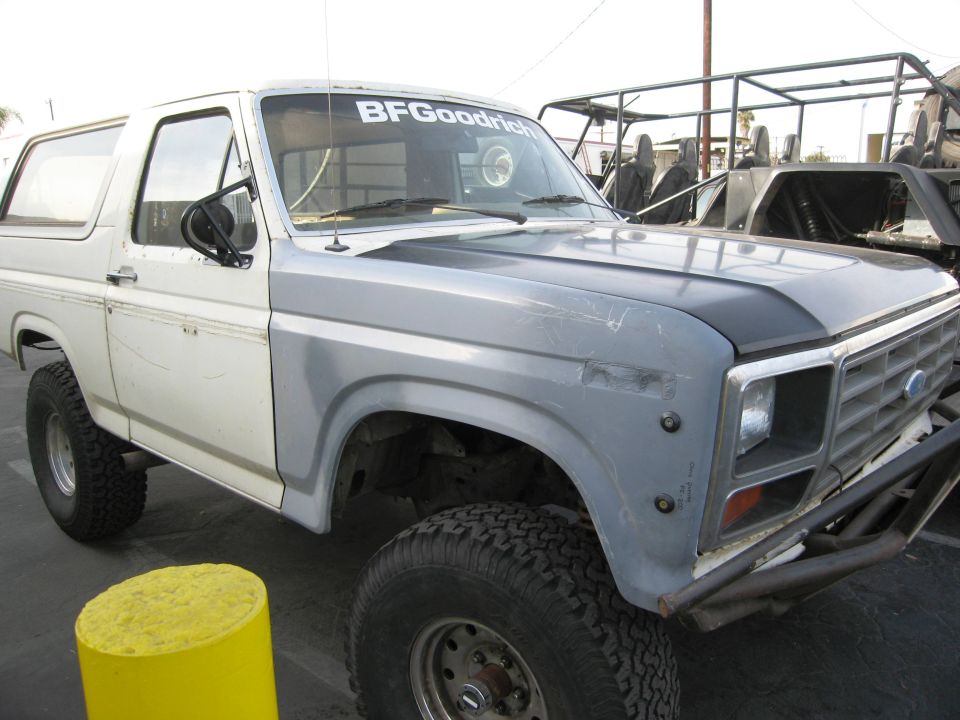 White and gray Ford Bronco with black hood and off-road tires in a lot