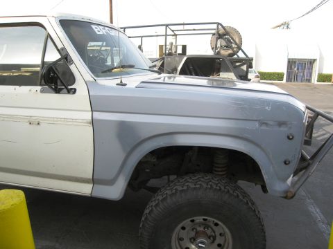 1986 Ford Bronco - Close side view of a white Ford Bronco fitted with a gray fiberglass one-piece front end with cut-out fender opening, showing the exposed c…