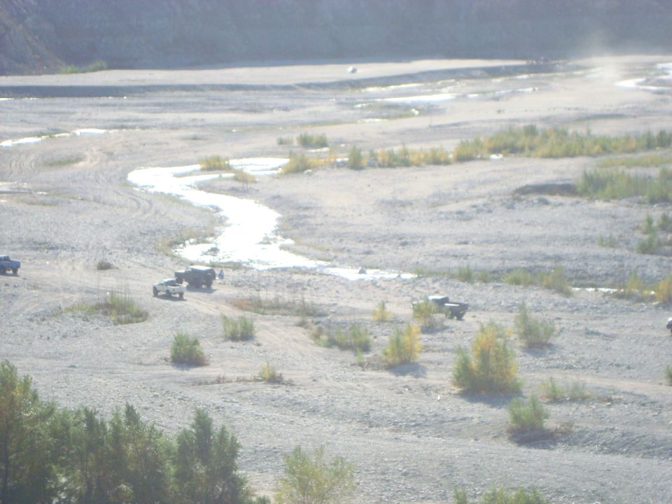 Several trucks navigate a rocky riverbed with a winding stream