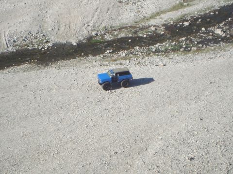 1986 Ford Bronco - A blue SUV with a tan soft top is parked on a gravelly surface, casting a shadow.