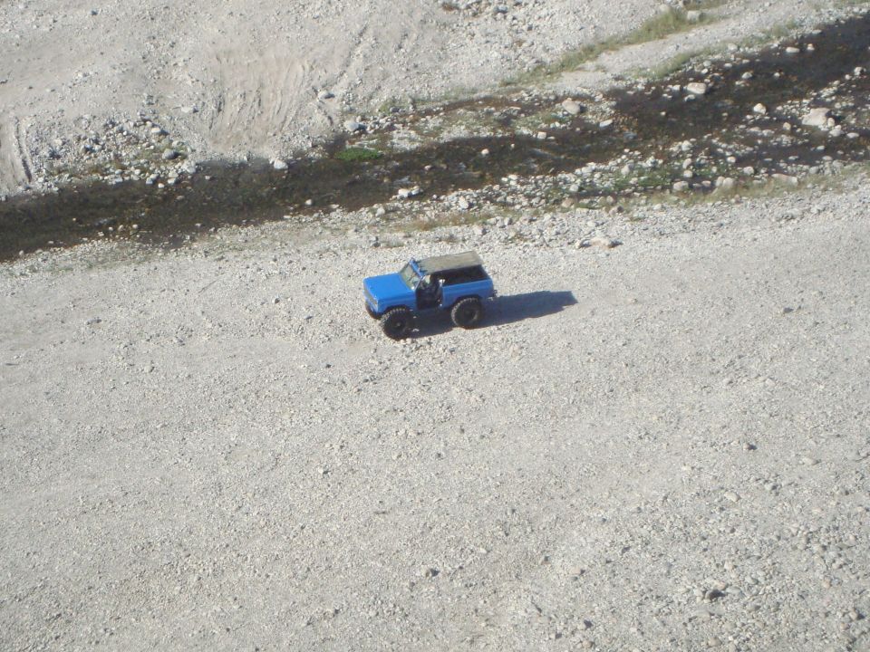 Blue SUV with a tan soft top, seen from above on a gravelly surface