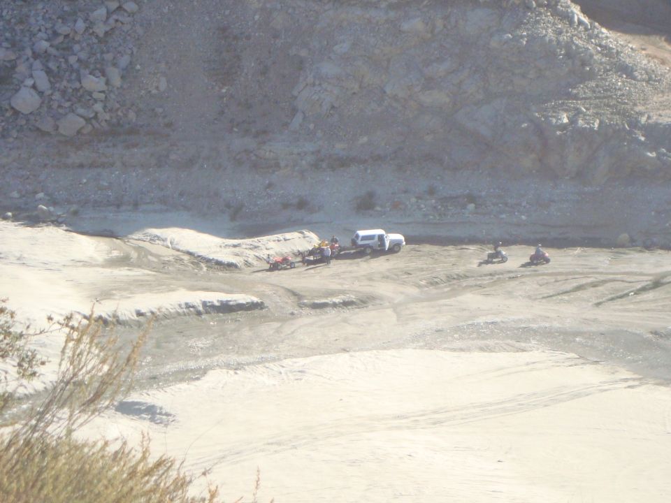 White SUV and ATVs in a dry, rocky landscape with a Supermotors.net watermark