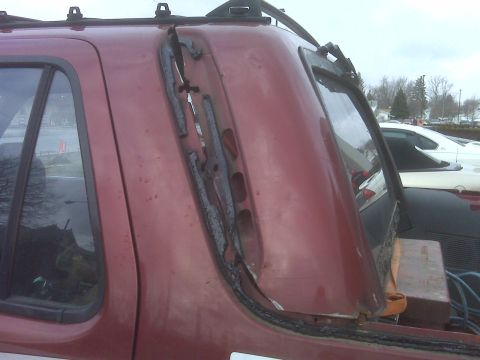1991 Ford Bronco - Close-up of damage to the roofline of a red SUV, with another vehicle visible in the background.