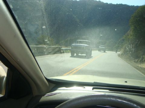 1986 Ford Bronco - A dark SUV is seen driving on a winding road, with another vehicle visible in the distance.
