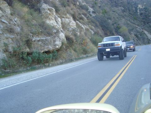 1986 Ford Bronco - A white Ford Bronco with a lifted suspension is seen driving on a mountain road, followed by another vehicle.