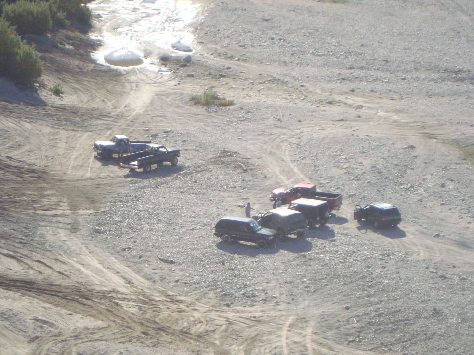 Several trucks and SUVs parked on a rocky, dry riverbed