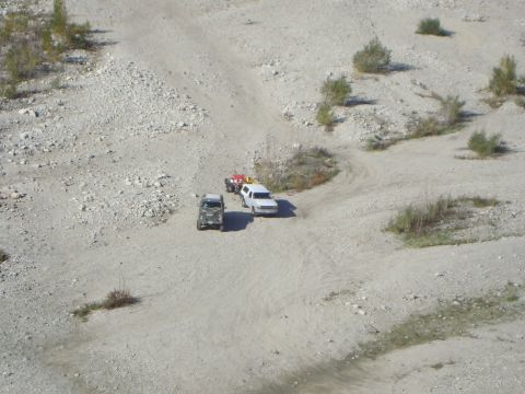 1986 Ford Bronco - Multiple off-road vehicles navigate a dusty quarry track under a bright sky.
