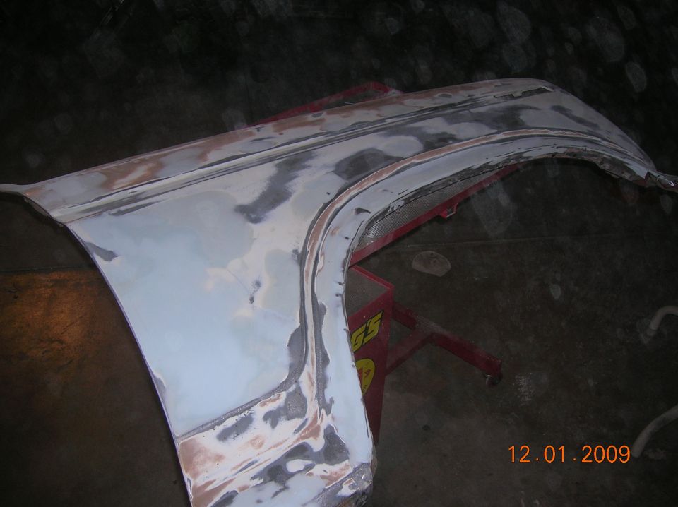 vehicle fender with body filler applied, resting on a red jack