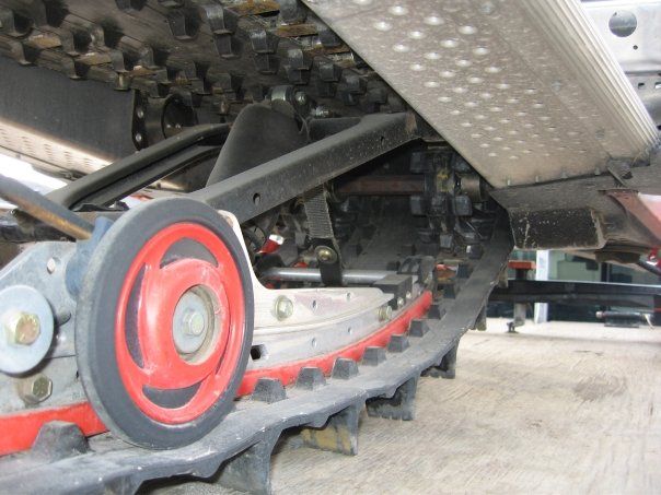 Underside of snowmobile track showing red drive wheel and suspension