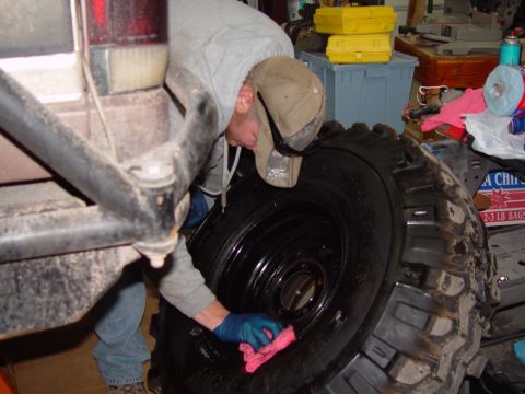 1993 Ford Bronco - Man cleaning a large off-road tire with a pink cloth in a garage.