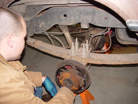1993 Ford Bronco - A mechanic works on the rear axle and brake assembly of a brown SUV, likely from the early 1990s.