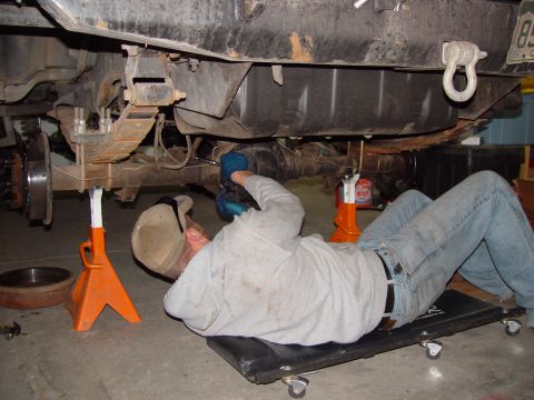 1993 Ford Bronco - Mechanic works on the rear axle of a 1993 Ford Bronco, supported by jack stands.