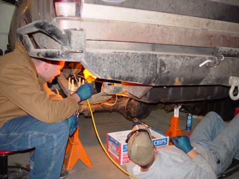 1993 Ford Bronco - Two mechanics are working on the rear axle of a 1993 Ford Bronco, which is supported by jack stands.