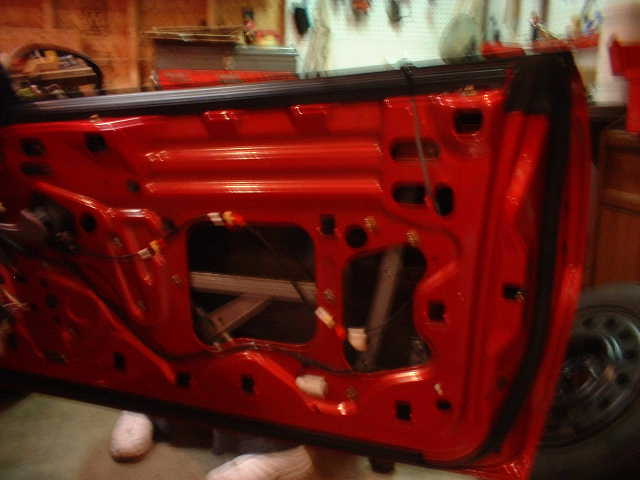 Red car door with interior trim panel removed showing window regulator and access holes