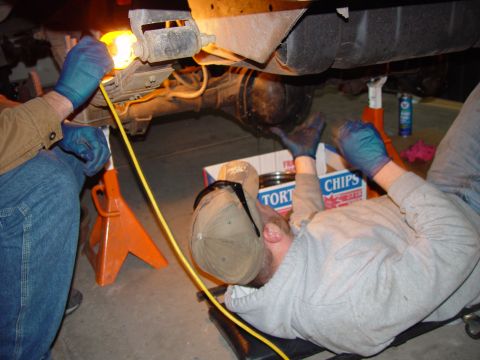1993 Ford Bronco - Two people are working on the rear axle of a vehicle, which is supported by jack stands.