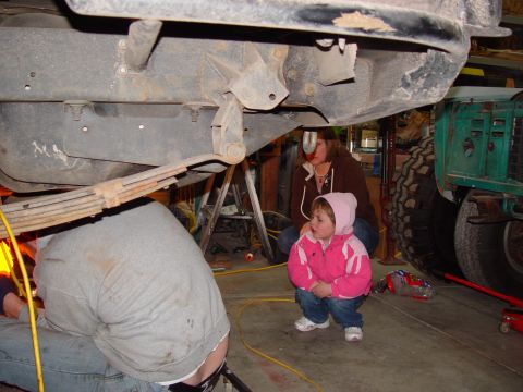 1993 Ford Bronco - A family observes as work is done on the undercarriage of a vehicle in a garage setting.