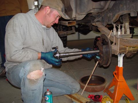 1993 Ford Bronco - Mechanic performing maintenance on a vehicle's rear axle assembly in a garage setting.