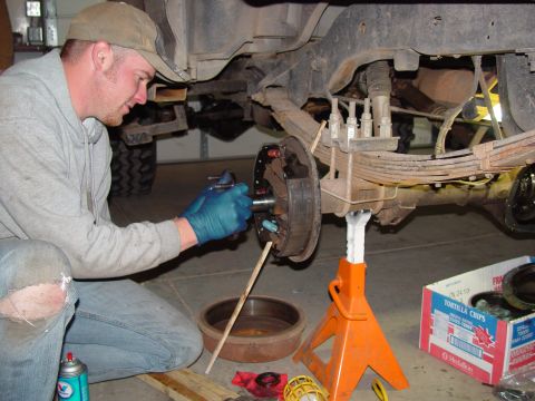 1993 Ford Bronco - A mechanic is shown servicing the rear brake assembly of a vehicle, with parts laid out nearby.