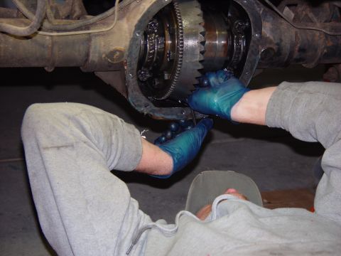 1993 Ford Bronco - Hands in gloves work on the gears inside a vehicle's differential assembly.