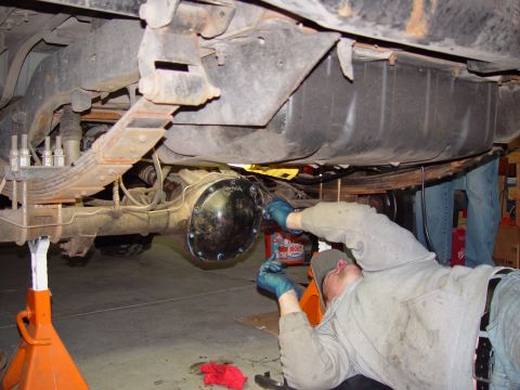 1993 Ford Bronco - Mechanic performs maintenance on the rear axle of a vehicle supported by jack stands.