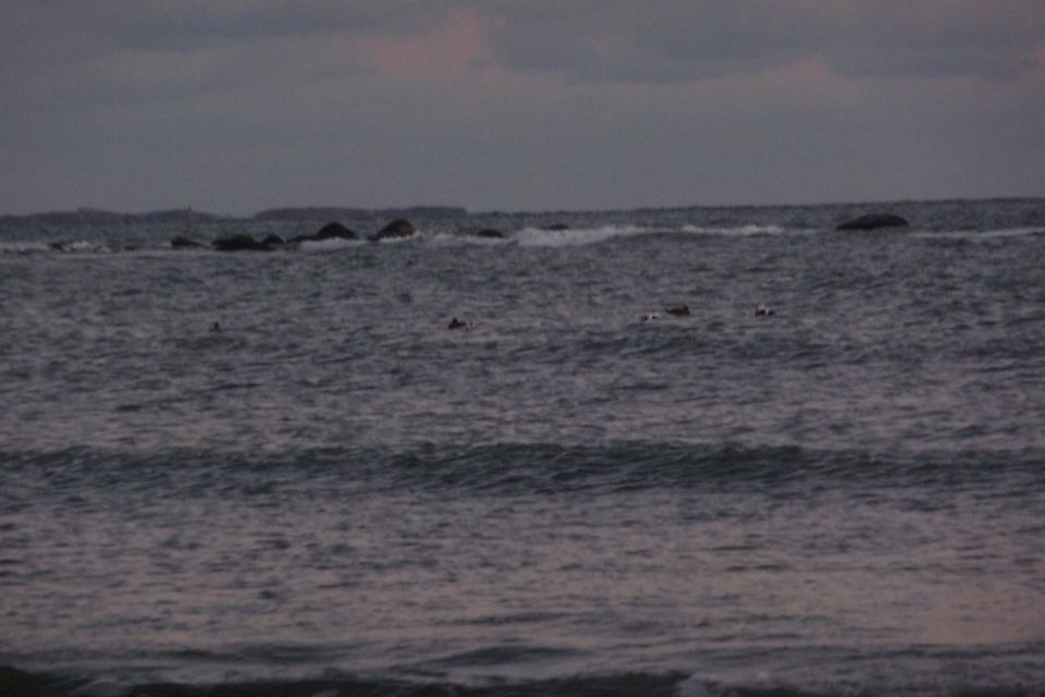 Ocean waves crash against rocks offshore under a cloudy sky