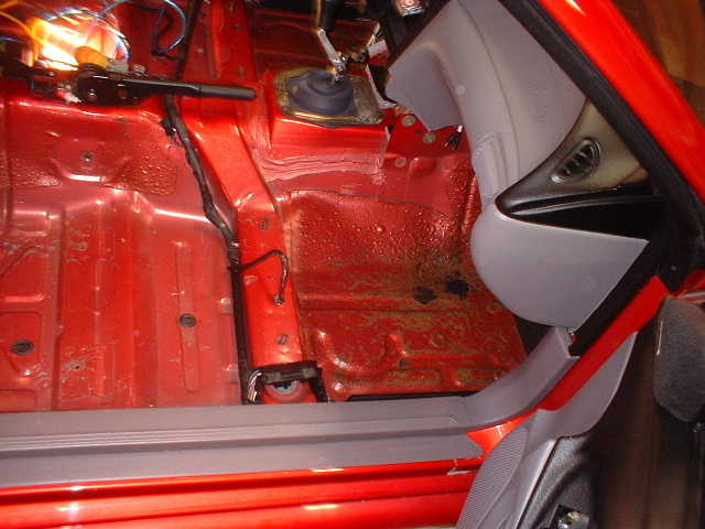 Stripped red floor pan seen through open door with grey door panel and window switches