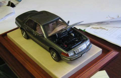 1999 Ford Crown Victoria - A detailed 1/18 scale model of a sedan sits on a display base, with its hood open to reveal the engine compartment.