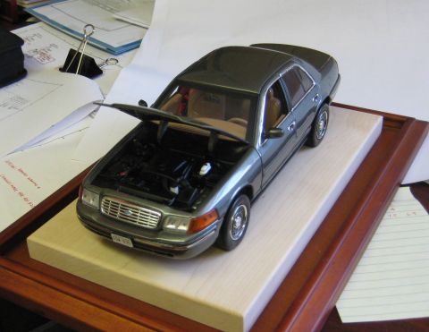 1999 Ford Crown Victoria - A 1998 Ford Crown Victoria model car is displayed on a wooden base with papers in the background.