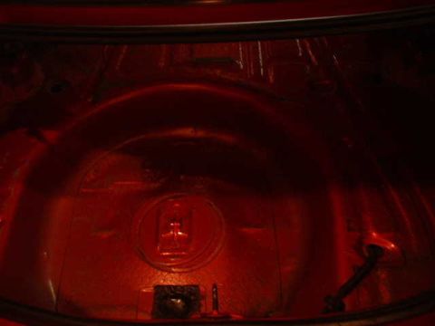 1994 Ford Mustang - The interior of a car trunk shows a red painted spare tire well and sound deadening material.