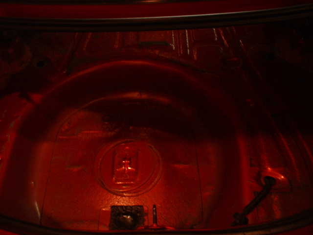 Empty red-painted trunk floor with spare tire well and hold-down bolt