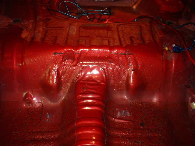 Stripped red car floorpan with exposed stampings and loose wiring