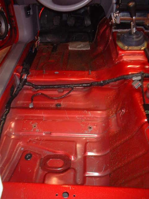 1994 Ford Mustang - Interior floor of a 1994 Ford Mustang after carpet removal, showing the red painted metal and wiring.