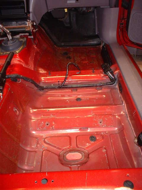 1994 Ford Mustang - The interior floor of a vehicle has been stripped bare, revealing the red metal and exposed wiring.