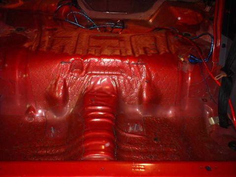 1994 Ford Mustang - The interior of a car shows exposed red metal flooring and wiring, with a ribbed tunnel in the center.