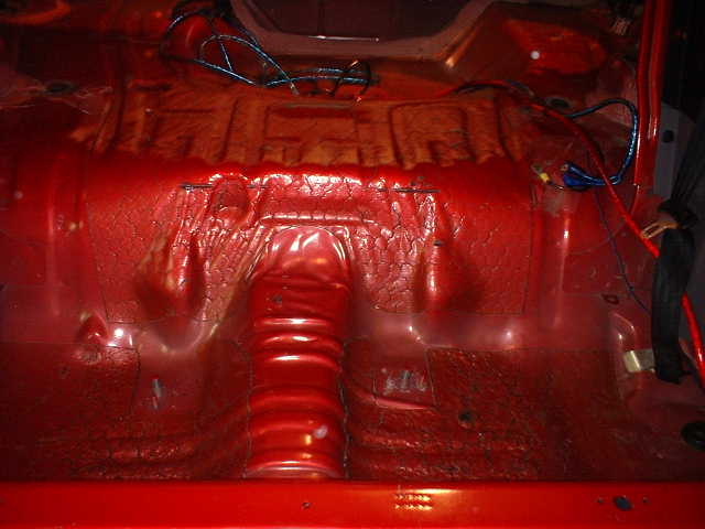 Gutted red car interior showing bare floorpan and loose wiring harness