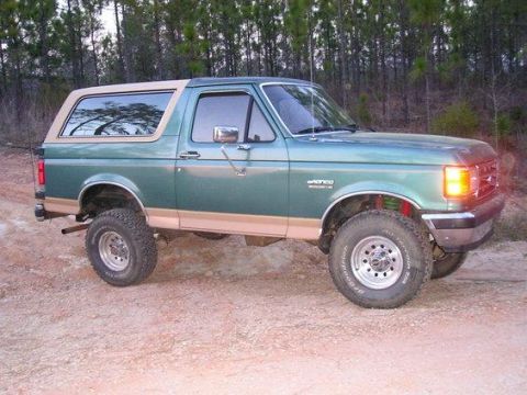 1989 Ford Bronco - Green 1989 Ford Bronco with tan trim and lifted suspension sits on a dirt road.