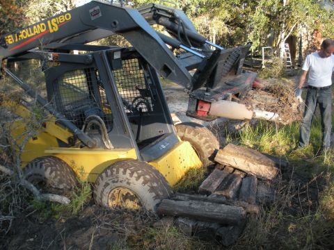 1996 Ford Bronco - A New Holland LS180 skid steer loader is stuck in the mud while a man stands nearby.