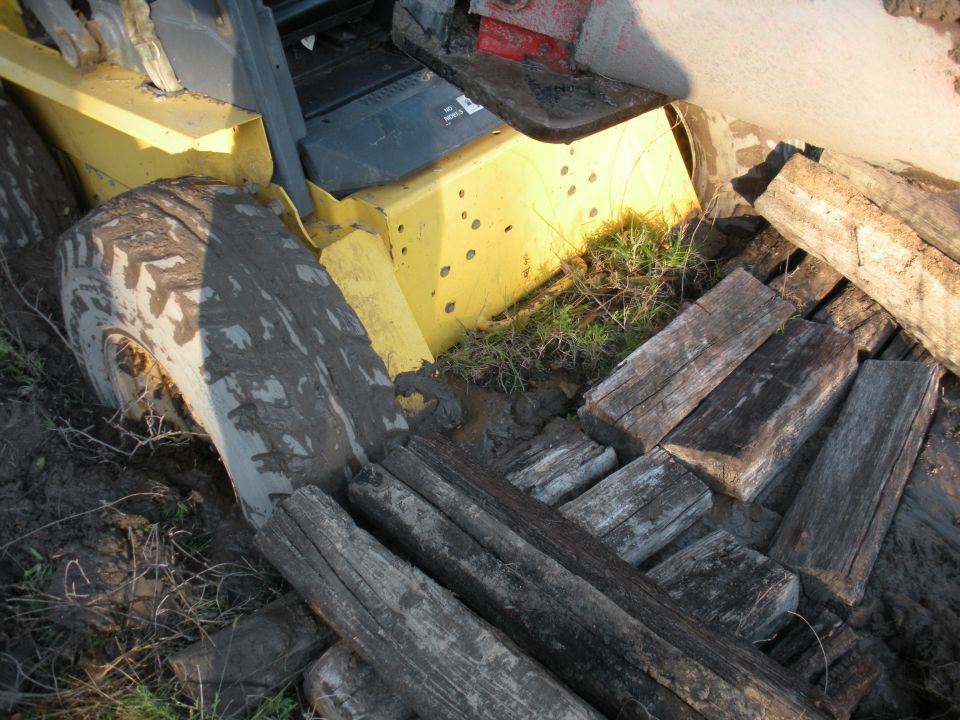 Yellow tractor stuck in mud with wooden planks nearby