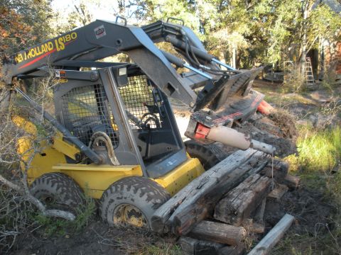 1996 Ford Bronco - New Holland LS180 skid steer loader with hydraulic breaker attachment is stuck in mud and logs.