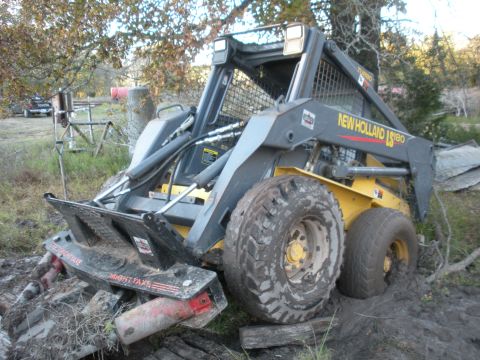 1996 Ford Bronco - A New Holland LS180 skid steer loader is stuck in the mud with its brush cutter attachment engaged.