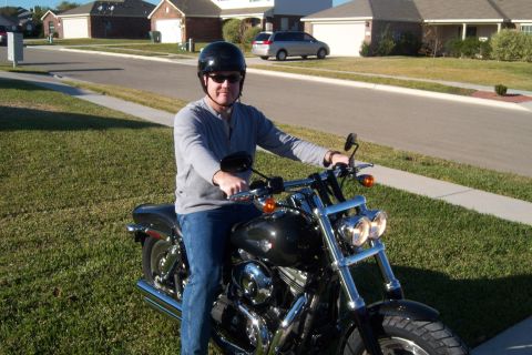 1996 Ford Bronco - A man is seated on a black motorcycle in front of houses and a street.