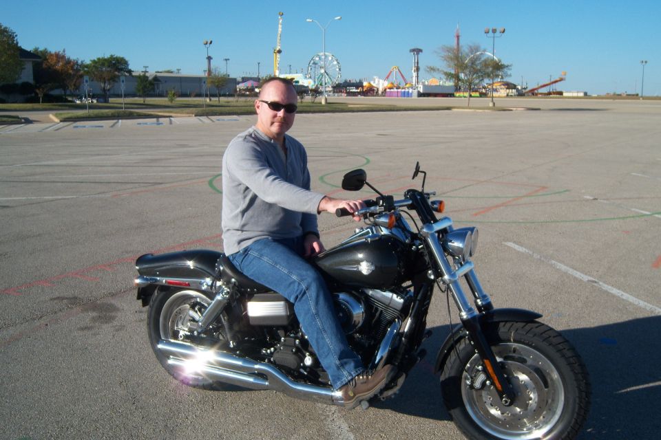 Man on a black motorcycle parked in a lot with a Ferris wheel in the background
