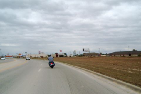 1996 Ford Bronco - A motorcycle rides down a highway under a cloudy sky, with commercial buildings visible in the distance.