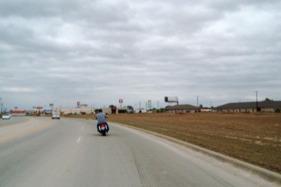 Motorcycle on highway with overcast sky and strip malls