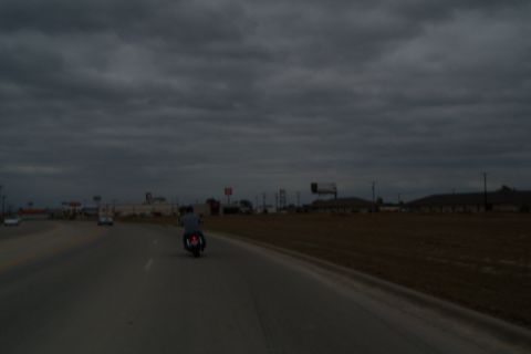 1996 Ford Bronco - A motorcycle rides down a highway with other vehicles in the distance under a cloudy sky.