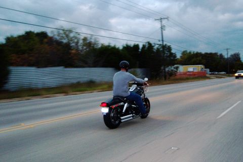 1996 Ford Bronco - A motorcycle with a rider travels down a highway under a cloudy sky.