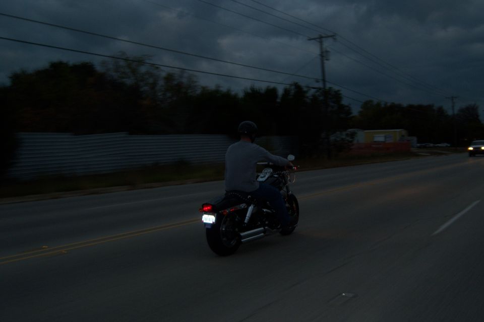 Motorcycle with rider on a road at dusk, rear view. Another car is visible in the distance
