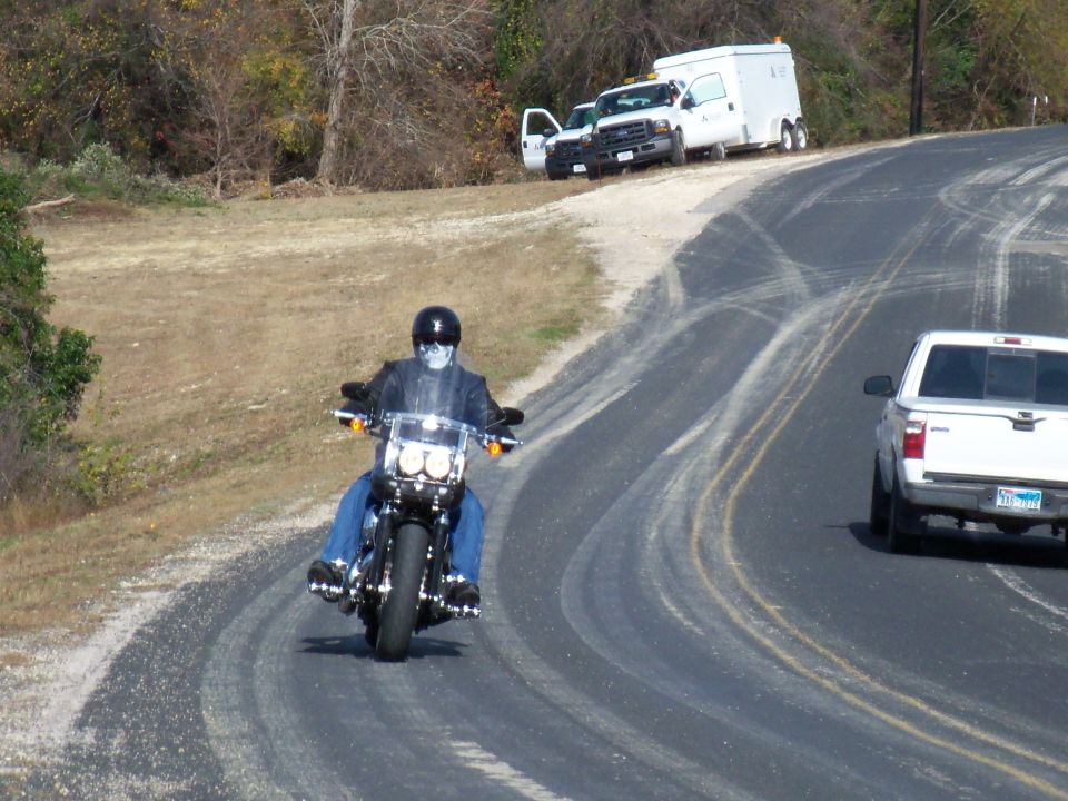 Motorcyclist with skull mask rides on a winding road with two trucks in background