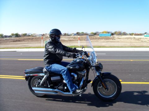 1996 Ford Bronco - A rider cruises down the road on a black Harley-Davidson motorcycle under a clear blue sky.