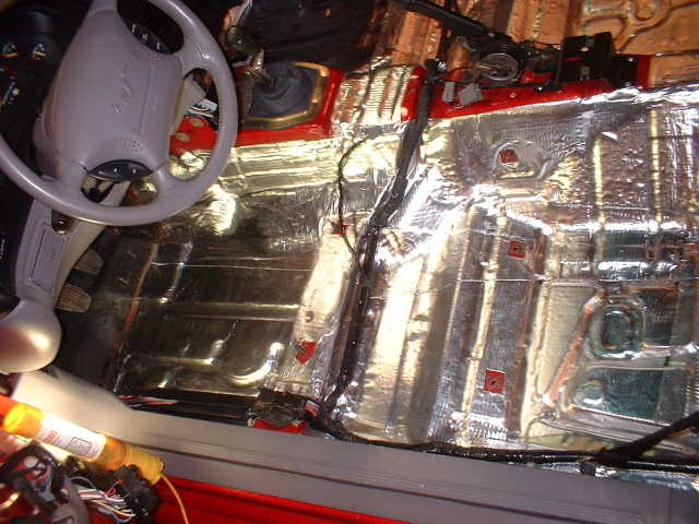 Driver side floor pan covered in foil sound deadening mat with grey steering wheel above